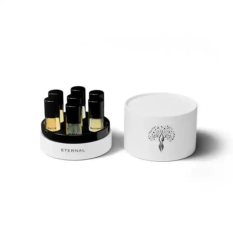 A set of six perfume oils vials with black caps and gold bases, displayed in a white circular stand next to its white lid, which features a black tree-like logo. The brand name 'ETERNAL' is printed on the stand.